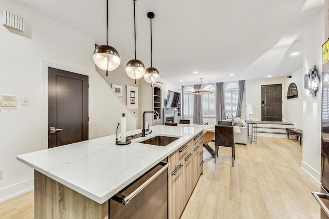 kitchen with sink, dishwasher, hanging light fixtures, light hardwood / wood-style floors, and a center island with sink