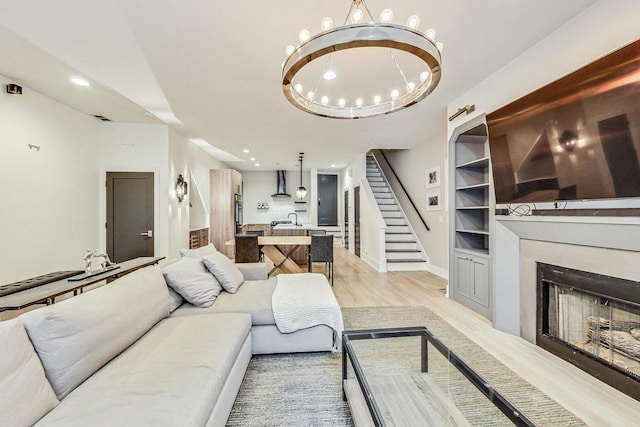 living room with a chandelier, built in shelves, and light hardwood / wood-style flooring