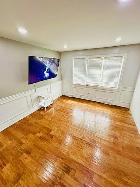 unfurnished living room with a wainscoted wall, recessed lighting, wood-type flooring, and a decorative wall