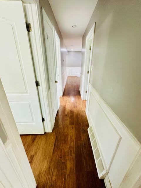 corridor with a wainscoted wall, wood finished floors, visible vents, and a decorative wall