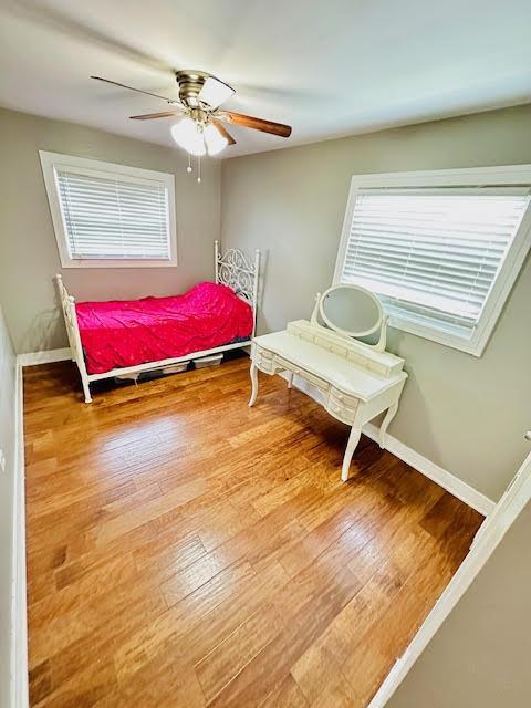 bedroom with ceiling fan, multiple windows, hardwood / wood-style flooring, and baseboards