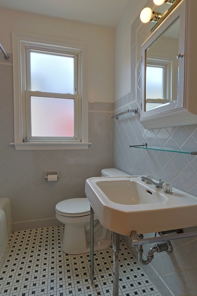 bathroom featuring toilet, a healthy amount of sunlight, tile patterned flooring, and tile walls