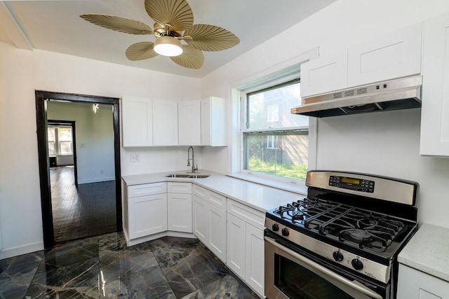 kitchen featuring stainless steel gas range oven, white cabinetry, sink, and ceiling fan