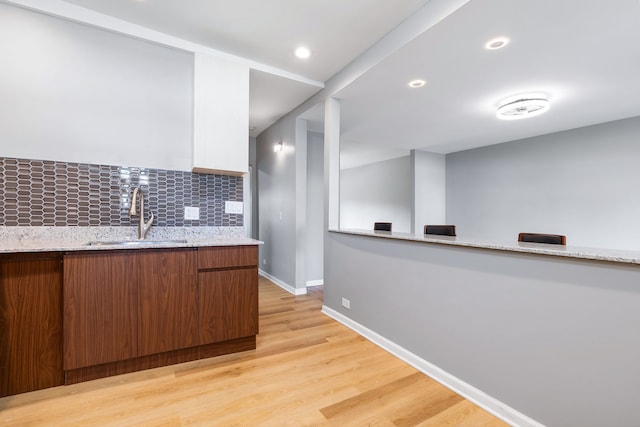 kitchen featuring light stone countertops, sink, tasteful backsplash, and light hardwood / wood-style flooring