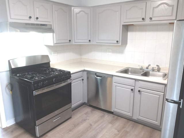 kitchen with stainless steel appliances, gray cabinetry, backsplash, light wood-type flooring, and sink