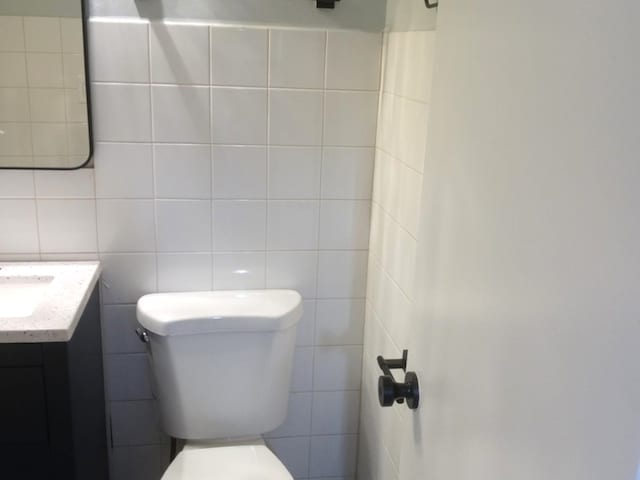 bathroom featuring toilet, tile walls, and vanity