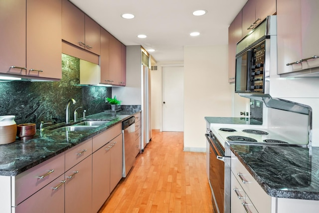 kitchen featuring stainless steel appliances, backsplash, light wood-type flooring, dark stone counters, and sink