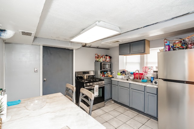 kitchen with light tile patterned flooring, sink, appliances with stainless steel finishes, a textured ceiling, and gray cabinetry