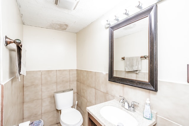 bathroom featuring vanity, tile walls, toilet, and a textured ceiling