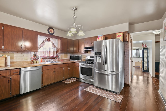 kitchen featuring appliances with stainless steel finishes, decorative light fixtures, dark wood-type flooring, and sink