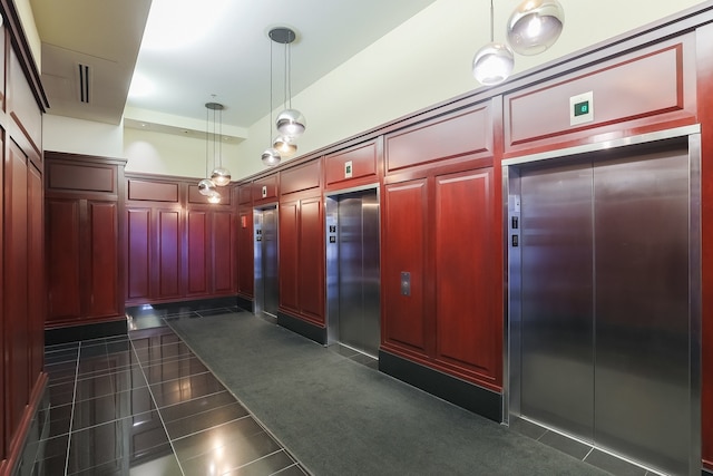 interior space featuring elevator, dark tile patterned floors, and hanging light fixtures