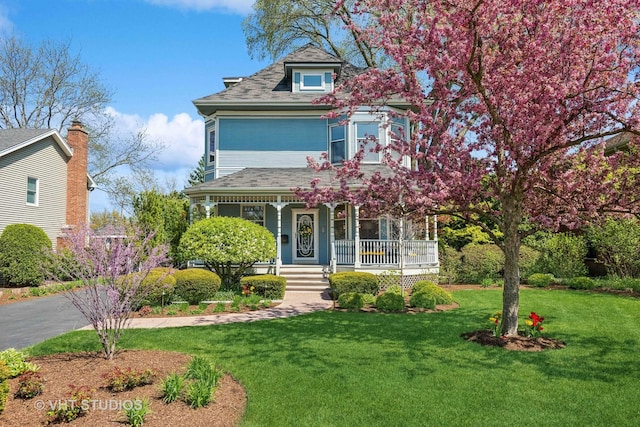 view of front of home featuring aphalt driveway, covered porch, and a front lawn