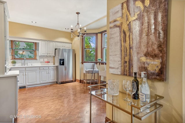 kitchen with stainless steel fridge with ice dispenser, light countertops, decorative backsplash, a notable chandelier, and a sink