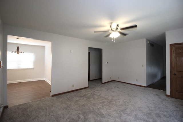 empty room with ceiling fan with notable chandelier and dark carpet