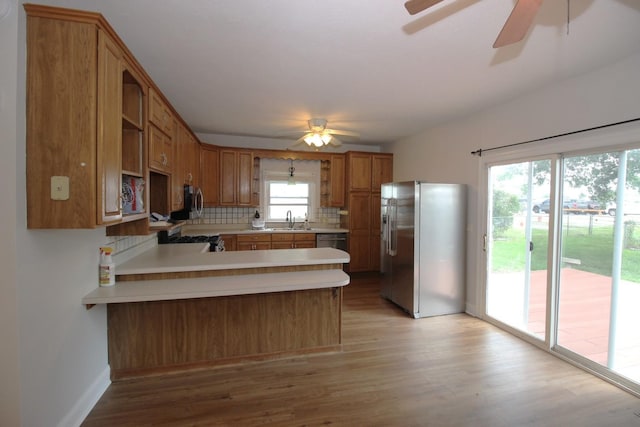 kitchen with kitchen peninsula, decorative backsplash, sink, light hardwood / wood-style flooring, and stainless steel appliances