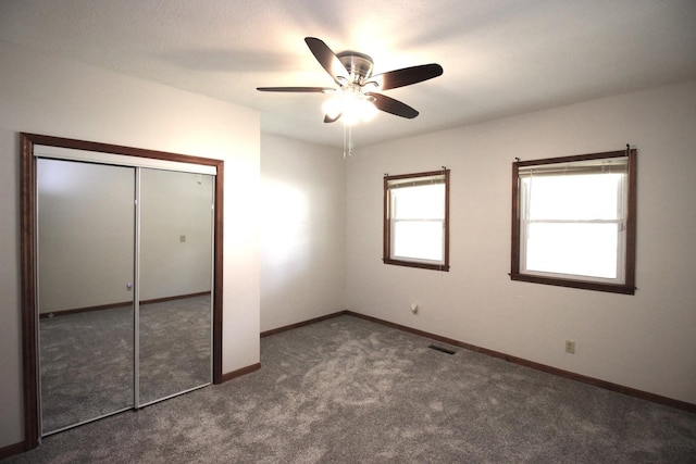 unfurnished bedroom with ceiling fan, dark carpet, and a closet