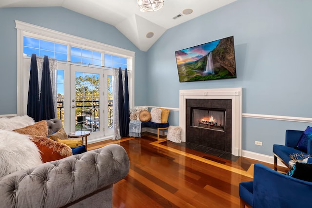 living room with a tiled fireplace, vaulted ceiling, and hardwood / wood-style floors