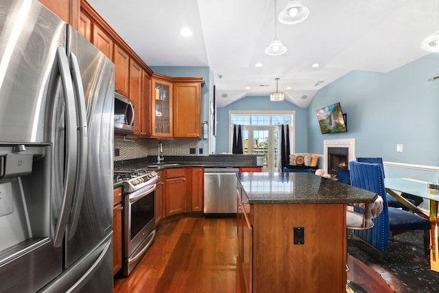 kitchen featuring appliances with stainless steel finishes, vaulted ceiling, dark hardwood / wood-style floors, decorative light fixtures, and a center island