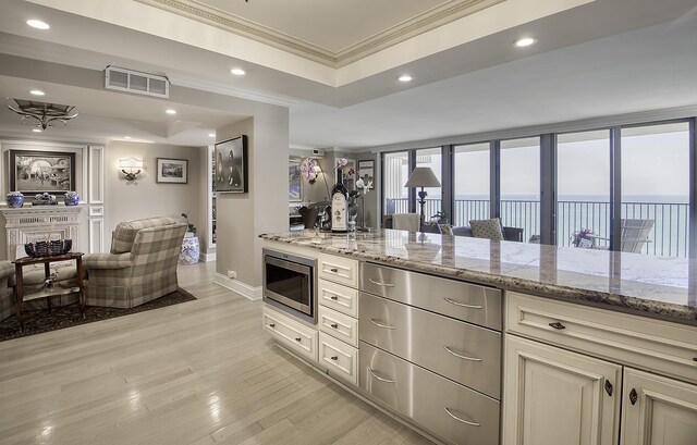 interior space featuring light stone counters, crown molding, light wood-type flooring, stainless steel microwave, and a water view