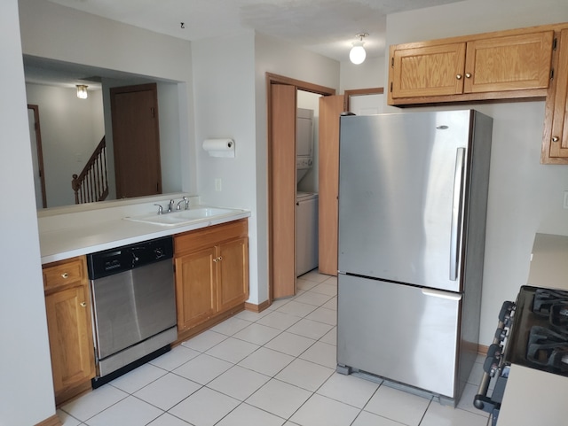 kitchen featuring stacked washer / drying machine, stainless steel appliances, sink, and light tile patterned flooring