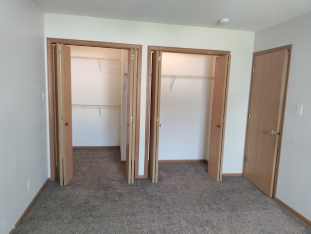 unfurnished bedroom featuring two closets and dark carpet