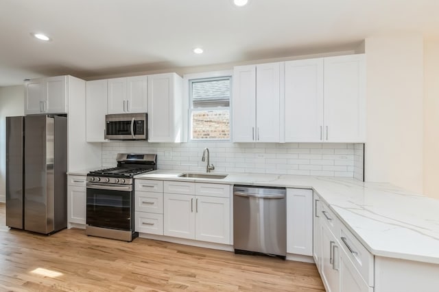 kitchen featuring tasteful backsplash, white cabinets, stainless steel appliances, light wood-type flooring, and sink