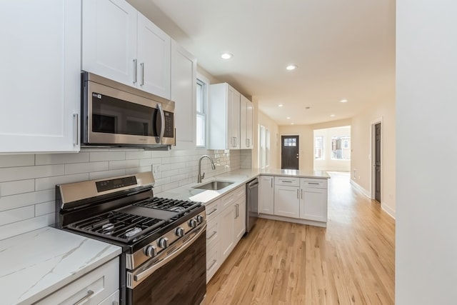 kitchen with sink, white cabinets, kitchen peninsula, light hardwood / wood-style flooring, and stainless steel appliances