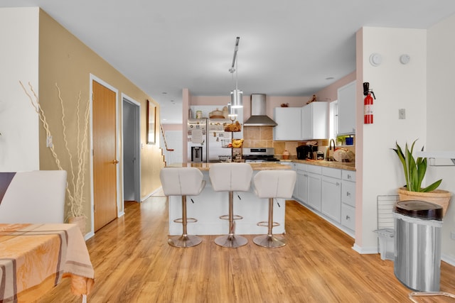 kitchen with pendant lighting, wall chimney exhaust hood, white cabinetry, appliances with stainless steel finishes, and a center island