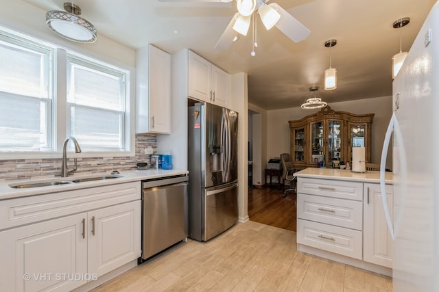 kitchen with sink, white cabinetry, hanging light fixtures, light hardwood / wood-style flooring, and stainless steel appliances