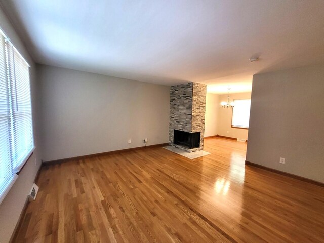 unfurnished living room featuring a stone fireplace, a chandelier, and wood-type flooring