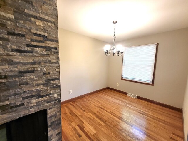 unfurnished dining area with a stone fireplace, an inviting chandelier, and hardwood / wood-style flooring