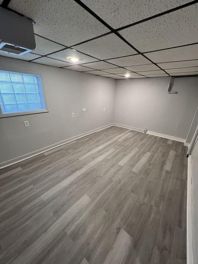 below grade area with a drop ceiling, wood finished floors, and baseboards