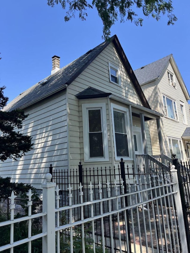 exterior space featuring roof with shingles, a fenced front yard, and a chimney