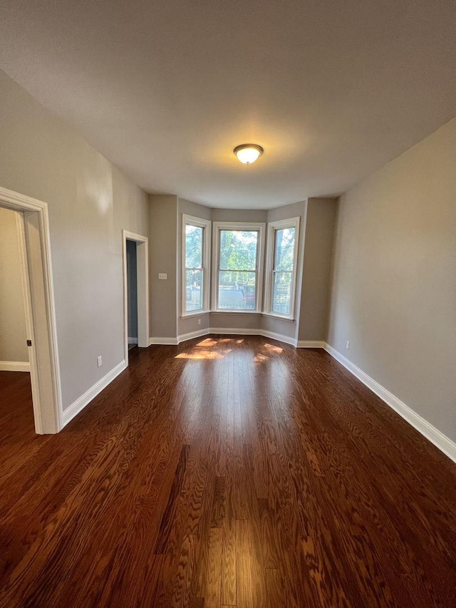 unfurnished room with dark wood-style flooring and baseboards