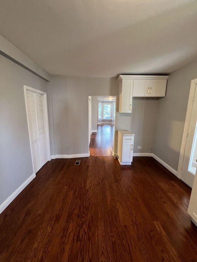 unfurnished room featuring dark wood-style flooring, visible vents, and baseboards