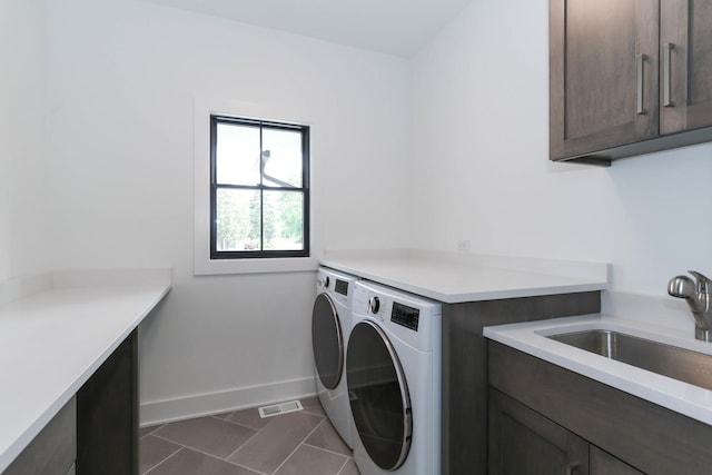 clothes washing area featuring cabinet space, a sink, separate washer and dryer, dark tile patterned flooring, and baseboards