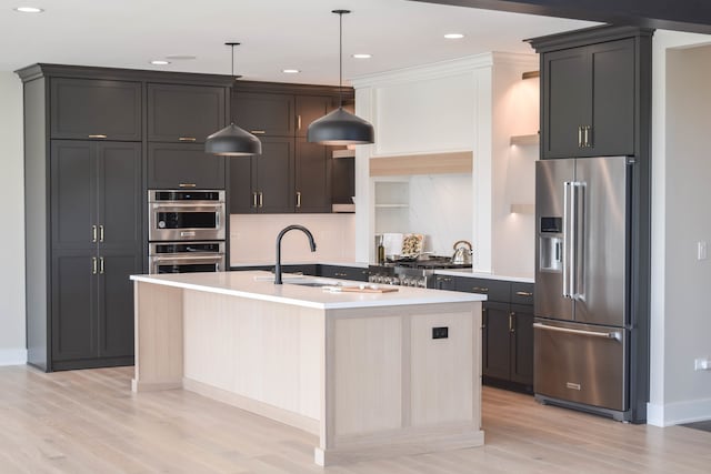 kitchen with an island with sink, stainless steel appliances, light hardwood / wood-style floors, pendant lighting, and sink