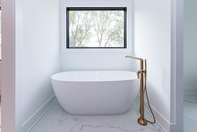 bathroom with a freestanding tub, marble finish floor, and baseboards