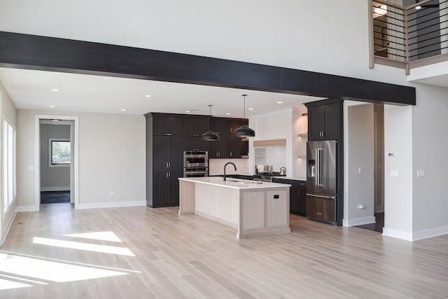 kitchen with an island with sink, open floor plan, hanging light fixtures, stainless steel appliances, and light countertops