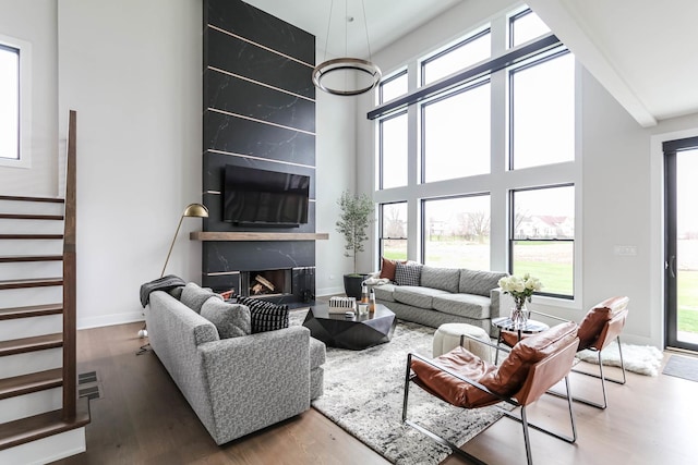 living area with a fireplace, stairway, a high ceiling, wood finished floors, and baseboards