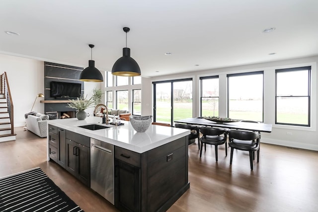 kitchen with a sink, open floor plan, light countertops, stainless steel dishwasher, and pendant lighting