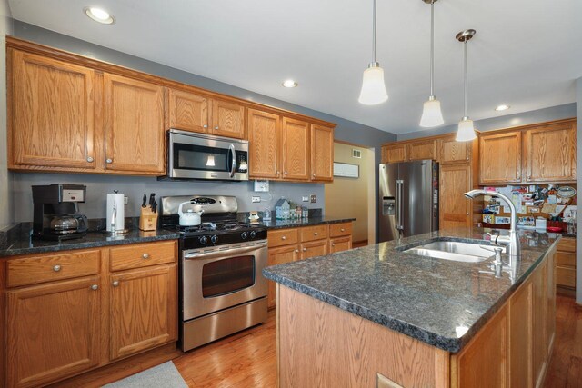 kitchen featuring stainless steel appliances, sink, pendant lighting, light wood-type flooring, and an island with sink