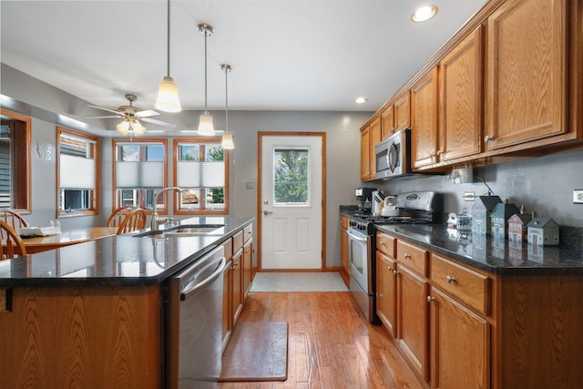 kitchen featuring light wood-type flooring, ceiling fan, appliances with stainless steel finishes, decorative light fixtures, and sink