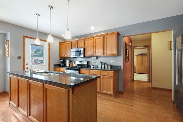 kitchen featuring appliances with stainless steel finishes, light hardwood / wood-style flooring, a center island with sink, sink, and decorative light fixtures