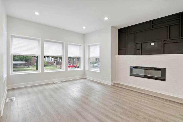 unfurnished living room with a brick fireplace and light wood-type flooring