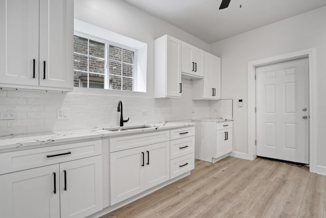 kitchen featuring white cabinetry, light stone counters, light hardwood / wood-style floors, decorative backsplash, and sink