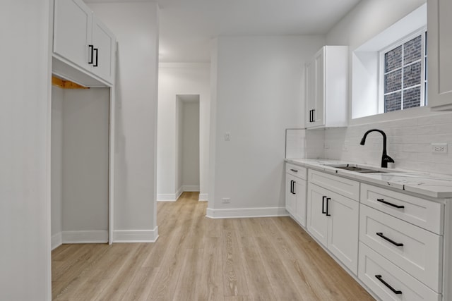 kitchen with light hardwood / wood-style floors, white cabinetry, decorative backsplash, and light stone counters