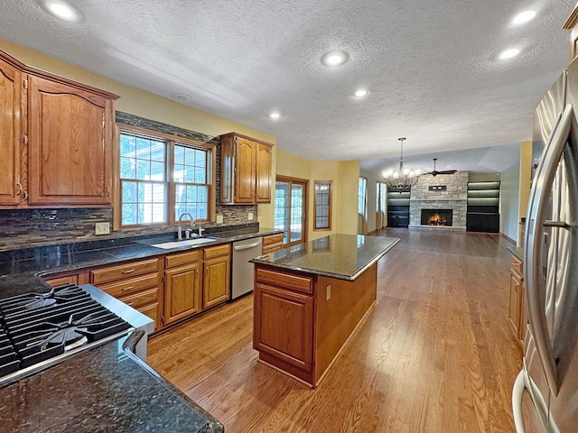 kitchen with light hardwood / wood-style flooring, stainless steel appliances, a kitchen island, tasteful backsplash, and a fireplace