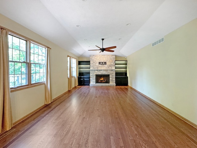 unfurnished living room with lofted ceiling, wood-type flooring, a stone fireplace, and ceiling fan