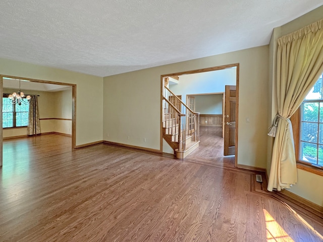 unfurnished living room with a notable chandelier, wood-type flooring, and a textured ceiling